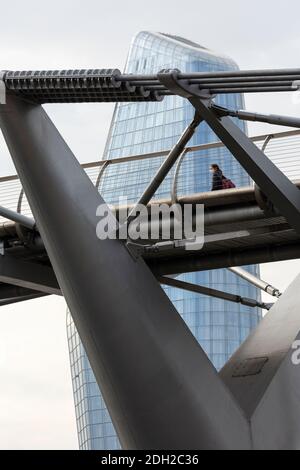 Vue en contre-angle d'une personne portant un masque de visage traversant le pont du Millénaire avec gratte-ciel derrière, Londres Banque D'Images