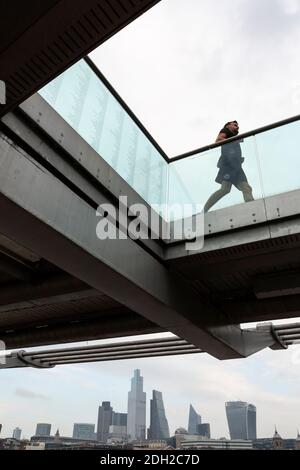 Vue en contre-angle d'un coureur s'exerçant sur le Millennium Bridge avec paysage urbain en arrière-plan, Londres Banque D'Images
