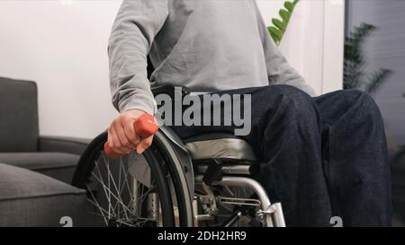 Homme en fauteuil roulant exerçant et levant du poids dans un salon. Banque D'Images