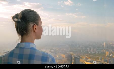 Femme regardant le paysage urbain à travers la fenêtre du gratte-ciel - arrière vue Banque D'Images