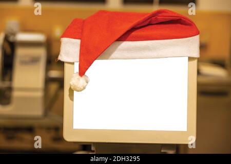 Gros plan sur une petite maquette blanche, tableau vierge avec chapeau de père Noël rouge sur le dessus. Concept d'arrière-plan des fêtes de Noël. Banque D'Images