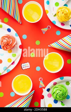 Configuration colorée de fête d'anniversaire avec des cupcakes et des boissons sur une nappe à pois Banque D'Images