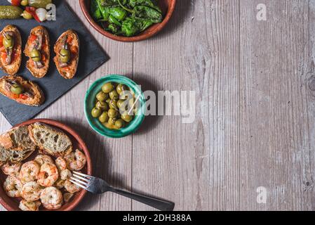 vue horizontale sur une table en bois préparée avec des ragoûts aux crevettes et poivrons verts, un plateau avec de petits toasts au poivron rouge et des anchois a. Banque D'Images
