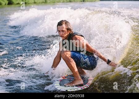 Belle wakesurf blonde aux cheveux longs en gilet à bord le long des vagues du lac. Un athlète sportif se réveille en surfant sur la rive en été Banque D'Images