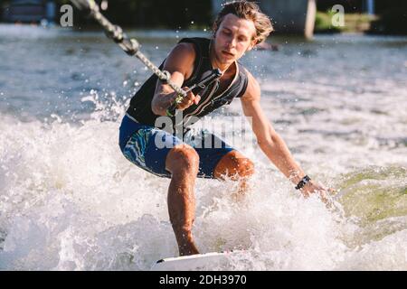 Belle wakesurf blonde aux cheveux longs en gilet à bord le long des vagues du lac. Un athlète sportif se réveille en surfant sur la rive en été Banque D'Images