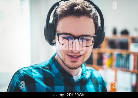 Écouter de la musique à la maison : un jeune homme du Caucase écoute de la musique avec un casque. Chemise à carreaux bleus. Banque D'Images