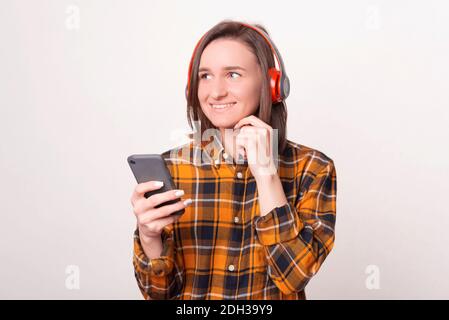 Une jeune fille heureuse écoute la musique à l'aide d'un casque et tient le téléphone sur fond blanc. Banque D'Images