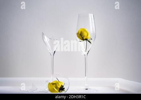 Deux verres de champagne avec une rose jaune sèche, un verre est cassé. Jaune et vert tendance 2021 couleurs. Banque D'Images