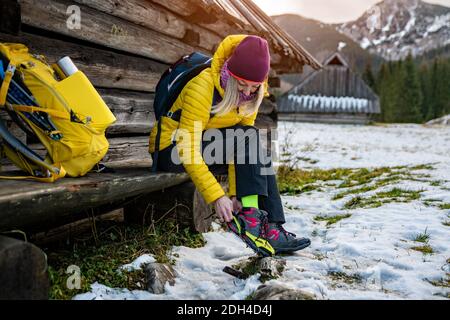 Femme blonde grimpante dans une veste jaune en duvet met des crampons sur ses chaussures avant d'atteindre le sommet. Banque D'Images