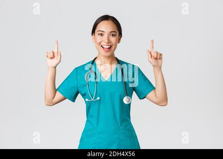 Covid-19, travailleurs de la santé, concept de pandémie. Souriant gai jolie infirmière, femme médecin ou interne dans les exfoliations pointant le doigt Banque D'Images