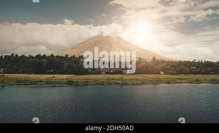 Le volcan éclate au soleil et brille au-dessus de l'antenne du bord du lac. Le pays de la ville de Legazpi, dans une vallée verdoyante avec des palmiers, est le plus proche des Philippines. Cottages ruraux dans une forêt exotique. Personne de cinéma nature paysage à la lumière du soleil Banque D'Images