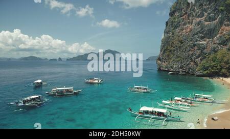 Paysage tropical sur une plage de sable avec des touristes au repos. Paysage majestueux de port à l'île d'El Nido, Philippines, Asie. Gros plan en bateau à passagers à la baie océanique avec falaise verte à la vue aérienne Banque D'Images