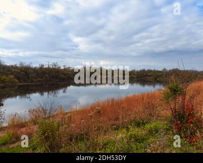 Scène de paysage de la fin de l'automne avec les couleurs d'automne toujours visibles lac calme avec ciel bleu et nuages reflétés dans le l'eau avec des arbres sans feuilles Banque D'Images