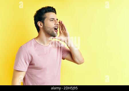 Jeune homme beau criant et criant fort à côté avec la main sur la bouche et l'espace de copie pour le texte Banque D'Images