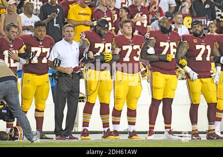 From left to right: Washington Redskins quarterback Colt McCoy (12), offensive guard Shawn Lauvao (77), head coach Jay Gruden, offensive tackle Ty Nsekhe (79), center Chase Roullier (73), offensive tackle Morgan Moses (76), and offensive tackle Trent Williams (71) lock arms in solidarity as the national anthem is sung prior to the game against the Oakland Raiders at FedEx Field in Landover, Maryland on Sunday, September 24, 2017. The Redskins chose to demonstrate prior to their nationally televised contest following tweets earlier in the day from United States President Donald J. Trump urging Stock Photo