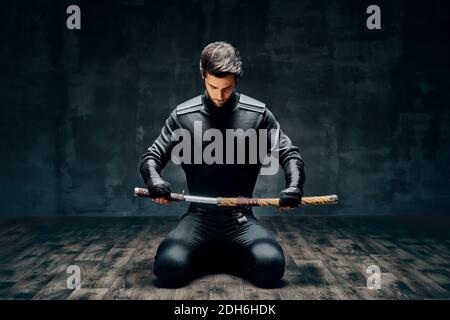 Homme guerrier assis sur le sol posant avec une épée Banque D'Images