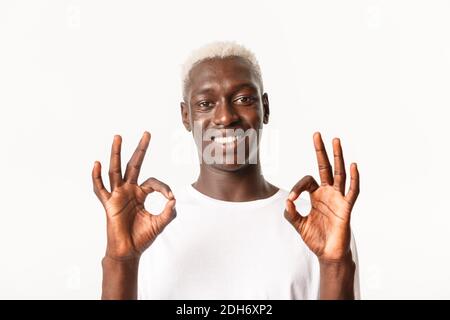 Gros plan d'un homme blond afro-américain séduisant et satisfait, qui fait preuve d'un bon geste et qui sourit, aime et approuve, se tenant au-dessus de wh Banque D'Images