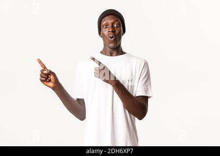 Portrait d'un homme afro-américain impressionné et surpris dans le beanie, pointant des doigts dans le coin supérieur gauche avec demandé, amusé fac Banque D'Images