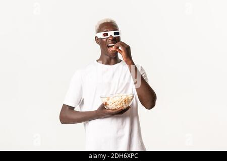 Portrait d'un beau gars afro-américain joyeux qui aime regarder un film en 3d, porter des lunettes et manger du pop-corn, debout Banque D'Images