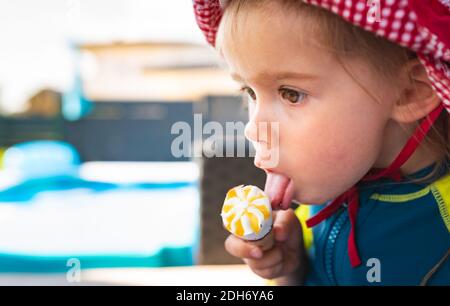 Portrait petit enfant avec de grands yeux léchant glace en été. bébé fille de 2 ans. Banque D'Images