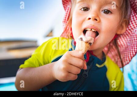 Portrait petit enfant avec de grands yeux léchant glace en été. bébé fille de 2 ans. Banque D'Images