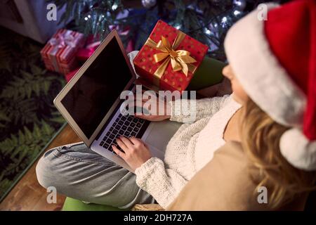 Bonne joyeuse femme dans le chapeau de Santa tapant quelque chose sur moderne appareil à la maison Banque D'Images