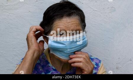 Une femme âgée met et fixe un masque de protection sur son oreille et son menton en touchant le masque avec les doigts. La vieille dame montre comment porter le masque de manière appropriée. ELD Banque D'Images