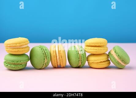 Pile de macarons ronds jaune et vert de farine d'amande avec de la crème sur fond bleu Banque D'Images