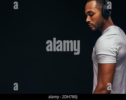 Homme musclé qui écoute de la musique avec un casque sans fil. Photo rognée de FIT MAN sur fond noir. Banque D'Images