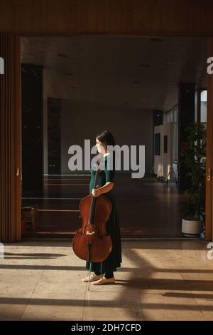 Adolescente avec son violoncelle, posant dans une salle. Banque D'Images