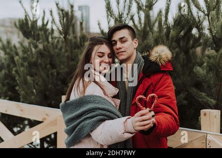 Un jeune couple tient une canne en sucre en forme de coeur et enserre. Portrait urbain des amoureux. Concept Noël, nouvel an et amour. Extérieur. Banque D'Images