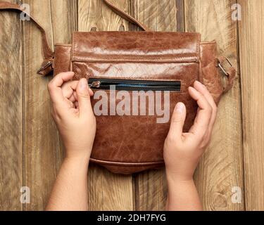 Deux mains femelles tiennent un sac en cuir marron sur un fond en bois gris Banque D'Images