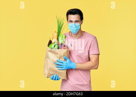 Homme tenant un sac de shopping en papier plein de légumes frais portant Masque et gants de protection pour COVID-19 Banque D'Images