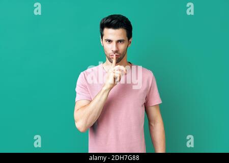 Jeune homme en t-shirt rose garde le doigt sur les lèvres, ce qui rend le geste de la hush isolé sur fond bleu Banque D'Images