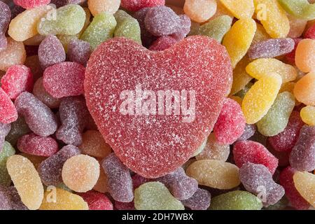 Un bonbon en forme de cœur sur un fond coloré de sucreries mélangées. Riche en sucre. Banque D'Images