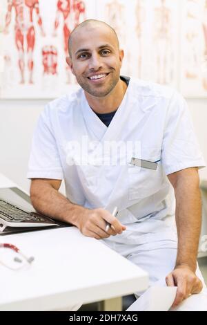 Portrait d'un médecin orthopédique homme heureux assis à son bureau clinique Banque D'Images