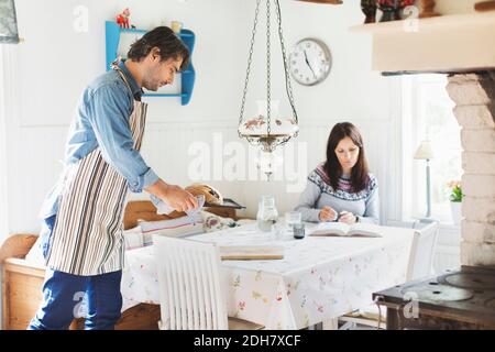 Vue latérale de l'homme servant du pain sur la table à manger pour femme à la maison Banque D'Images