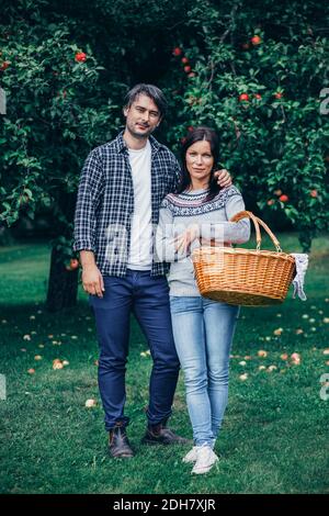 Portrait d'un couple debout avec un panier en osier dans un verger de pomme Banque D'Images