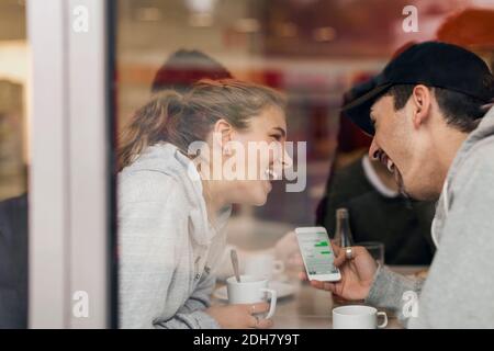 Vue d'un jeune couple heureux utilisant un smartphone dans un café à travers le verre Banque D'Images