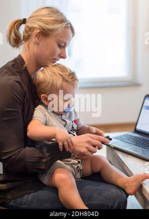 Mère avec bébé garçon utilisant le téléphone portable à la maison Banque D'Images