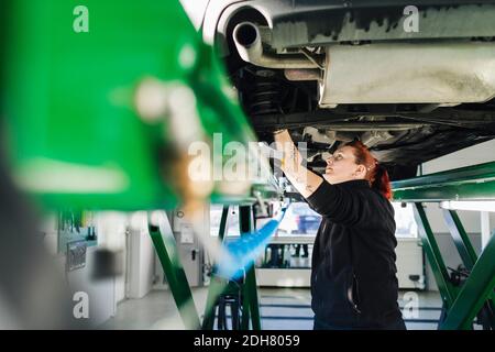 Vue latérale d'une femme mécanicien répare la voiture sur un relevage hydraulique Banque D'Images