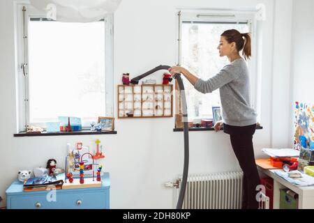 Femme passant l'aspirateur sur de petites étagères Banque D'Images