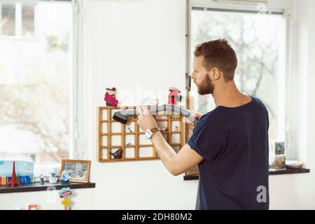 Jeune homme passant l'aspirateur sur de petites étagères à la maison Banque D'Images