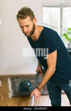 Jeune homme passant l'aspirateur à la maison Banque D'Images