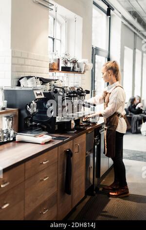 Toute la longueur d'une femme Barista utilisant une machine à café au café Banque D'Images