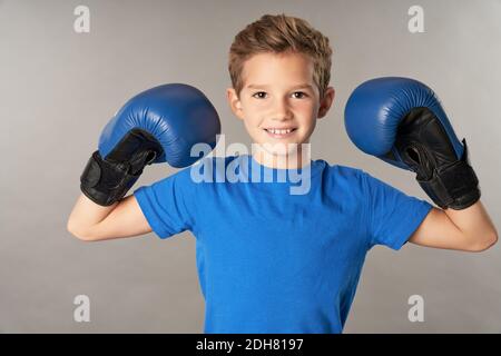 Adorable boxeur pour enfants, portant des gants de boxe et du bleu en regardant l'appareil photo et en souriant Banque D'Images