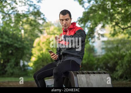 Homme assis sur un banc tenant le téléphone regardant la montre-bracelet Banque D'Images