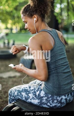 Femme utilisant un smartphone et regardant la montre-bracelet dans le parc Banque D'Images