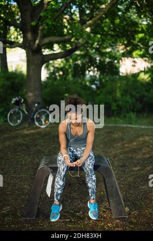Femme assise au banc pour écouter de la musique dans le parc Banque D'Images