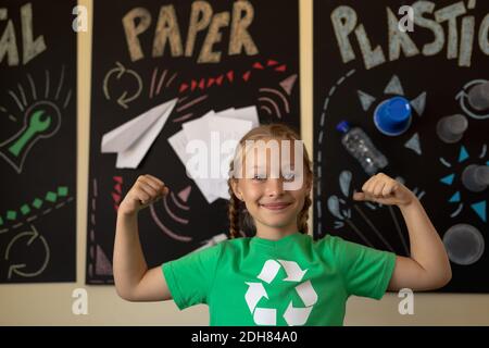 Écolière portant un t-shirt vert avec un logo de recyclage blanc sur lui et fléchit ses biceps Banque D'Images